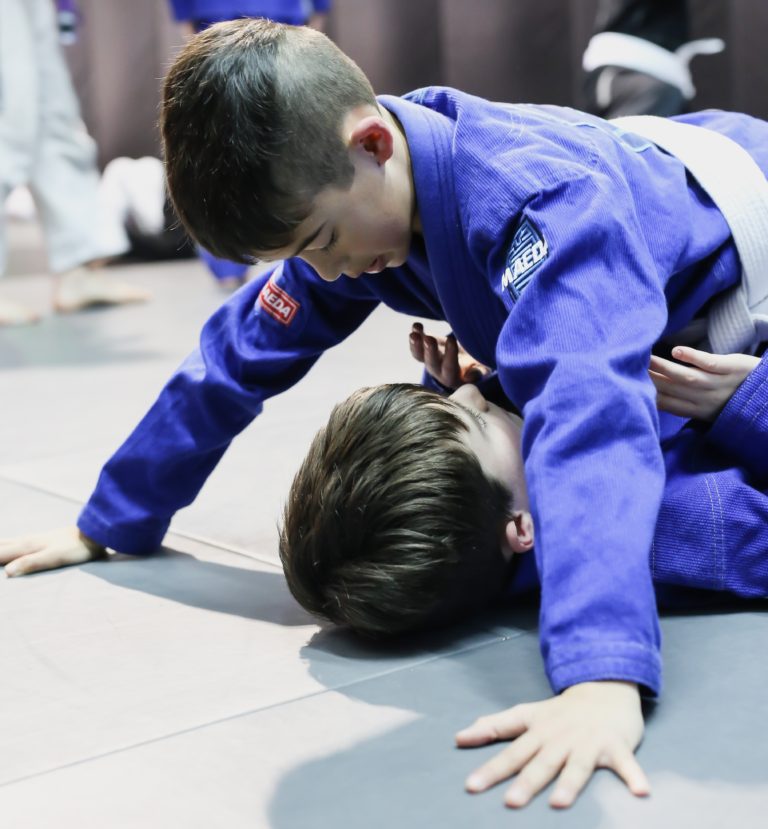 Two young students rolling on the mats in kids BJJ class
