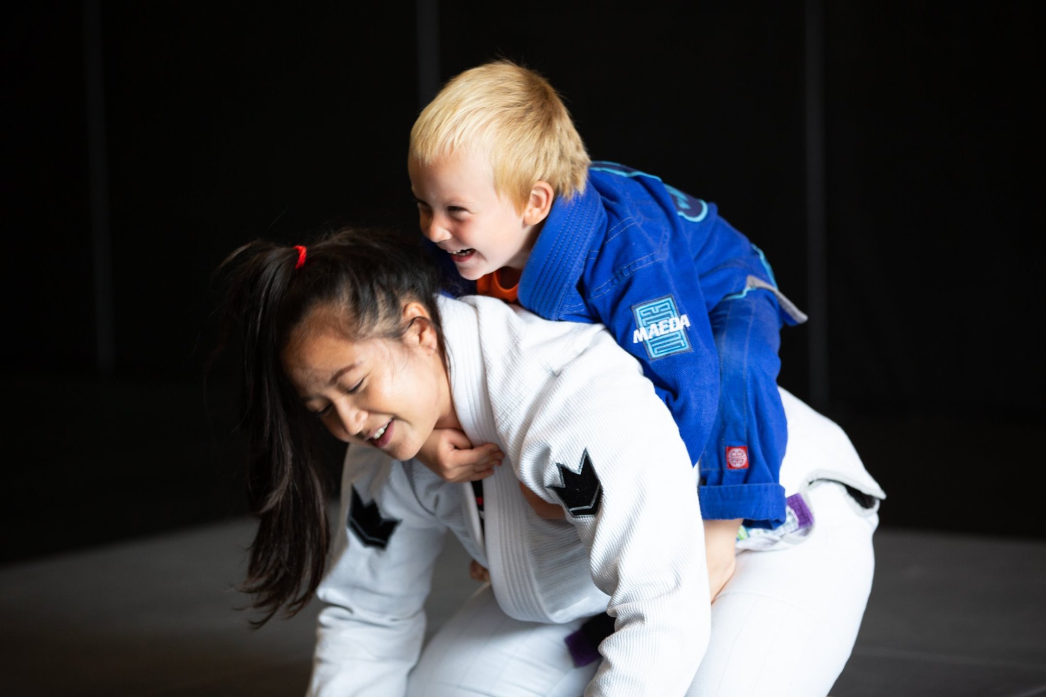 Young Van Isle BJJ student smiling on a coach's back during kids class